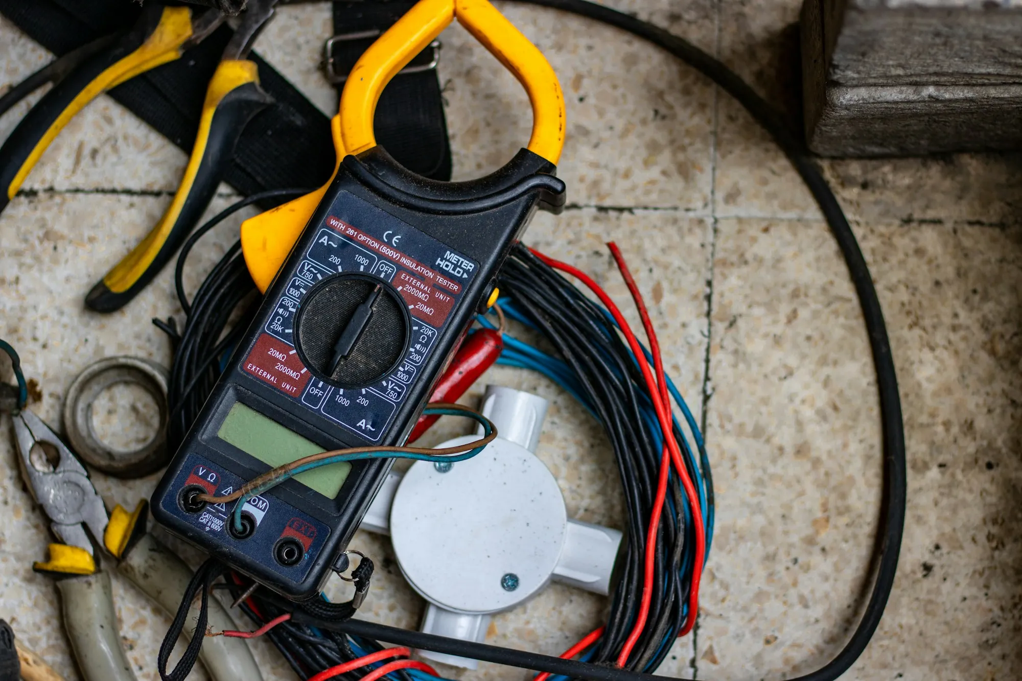 A multimeter and hand tools laid out beside electrical cable