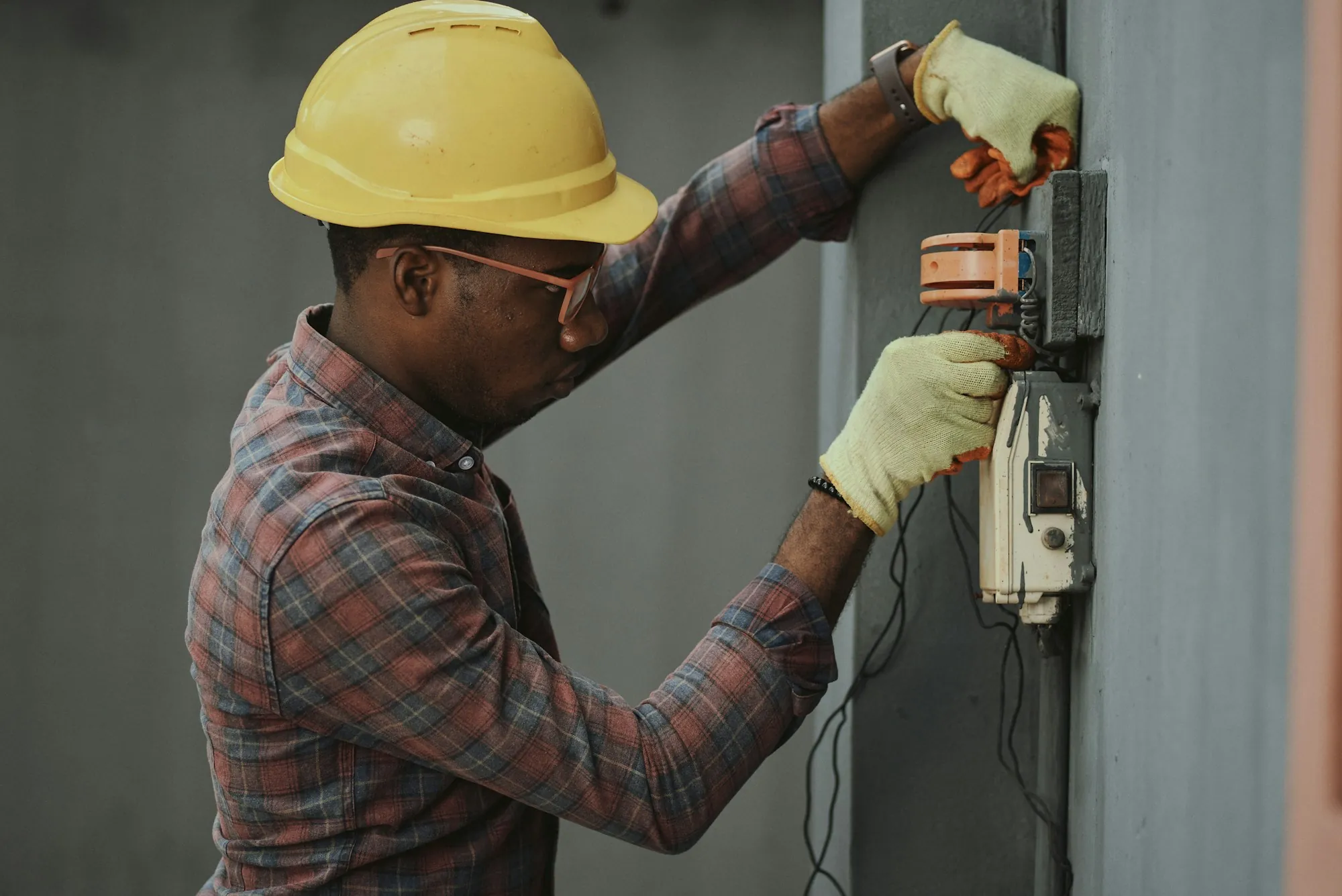 Electrician in safety glasses testing connections at an exterior meter box