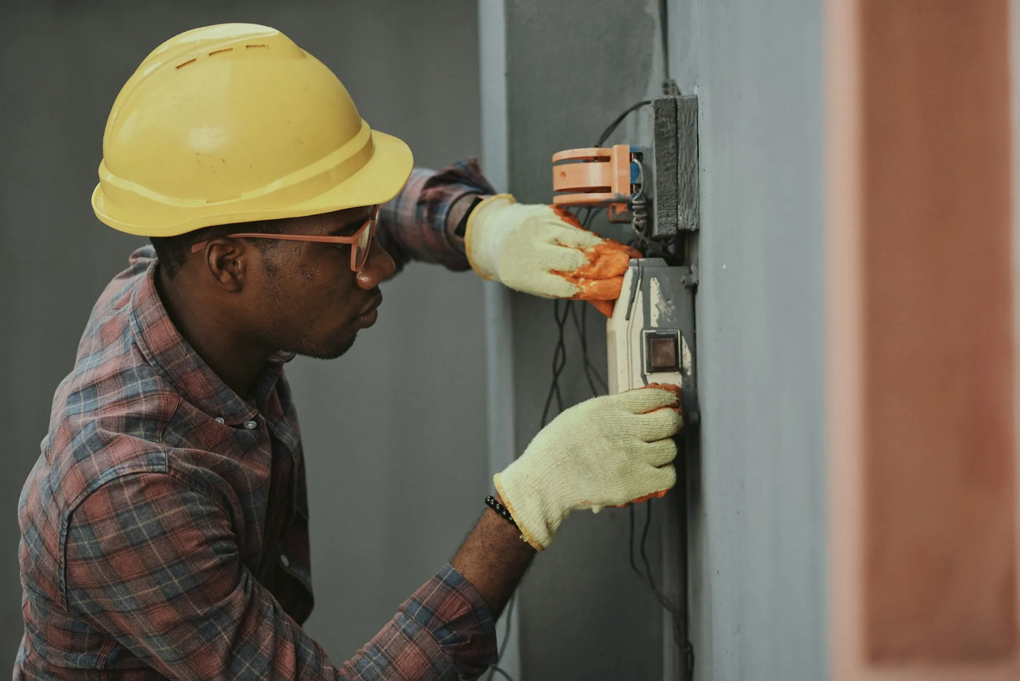 Electrician in a hard hat and work gloves wiring a meter box on an outside wall